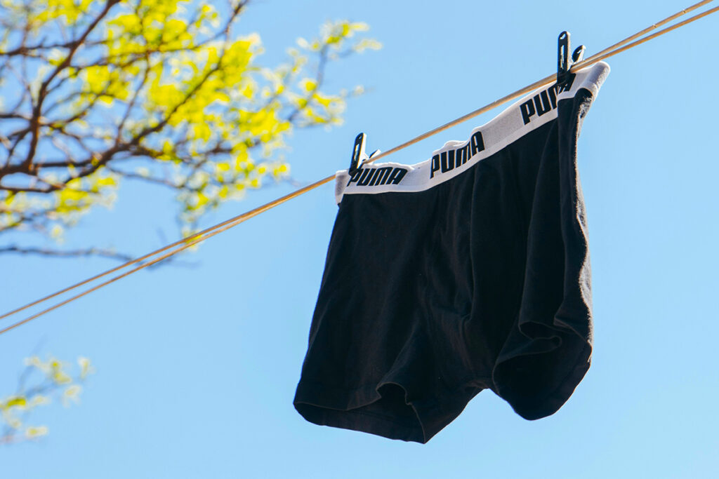 A pair of black boxer briefs hang from clothes line against a blue sky.