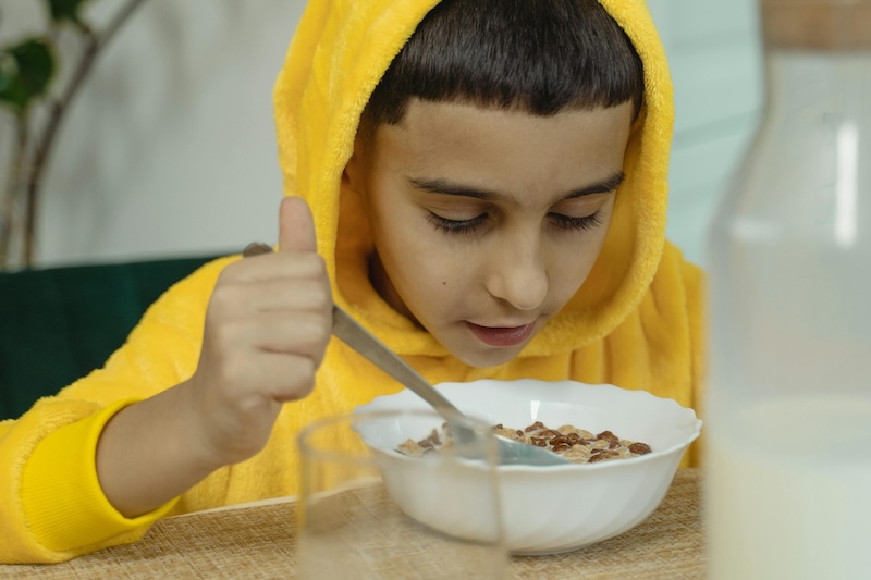 Child with yellow hoodie eating cereal