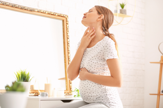 A pregnant person looking in the mirror and applying face cream.