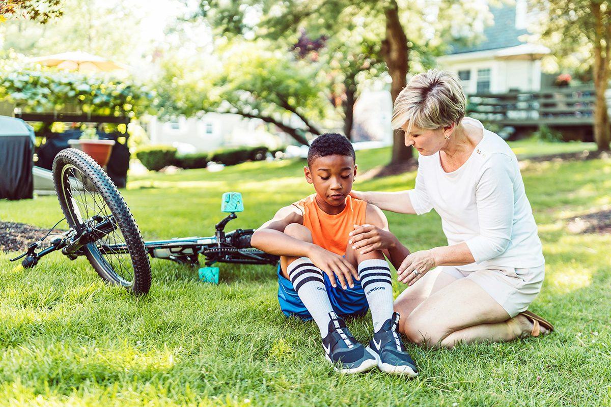 kid falling from bike and holding the leg while an adult is checking