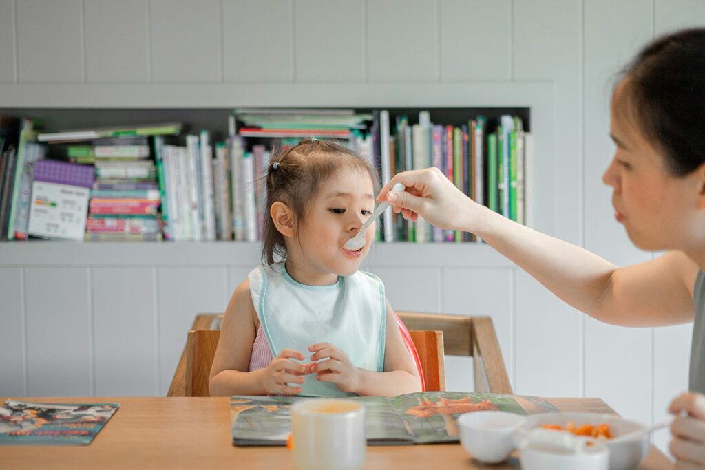 an adult giving food to a kid using spoon