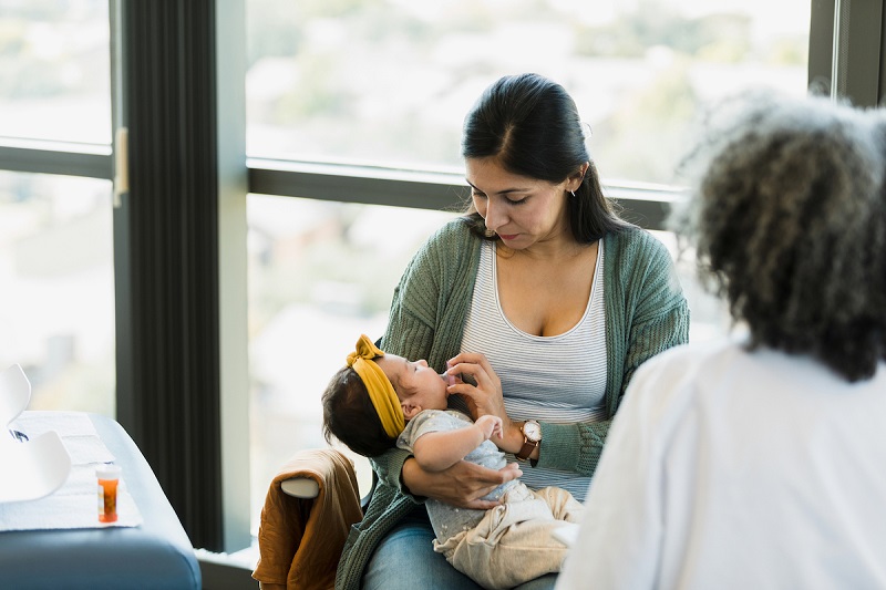 A parent looks down at a fussy baby during a well-baby visit after birth.