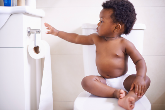 Toddler sitting on top of toilet reaching for toilet paper.