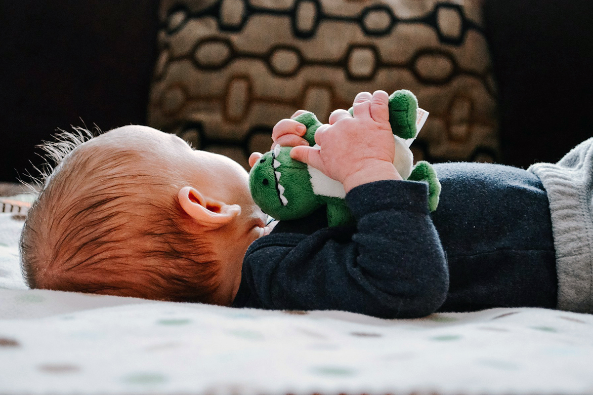 kid laying on bed with stuffed toy in hand