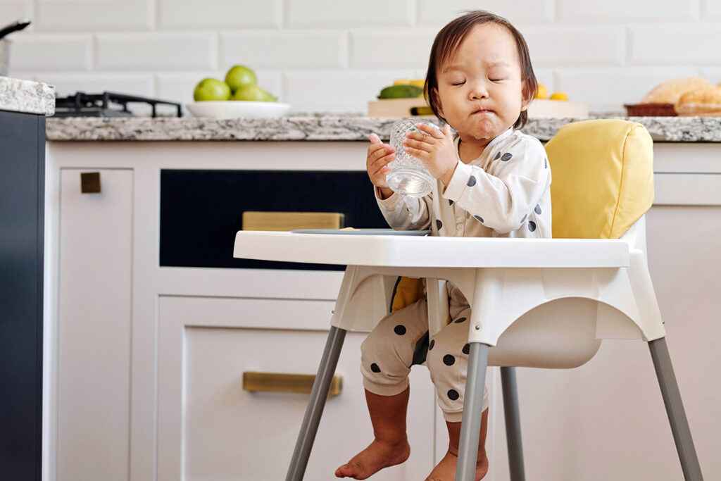 toddler sitting on a high chair and drinking water