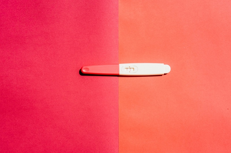 A positive pregnancy test is seen on a pink and orange background.