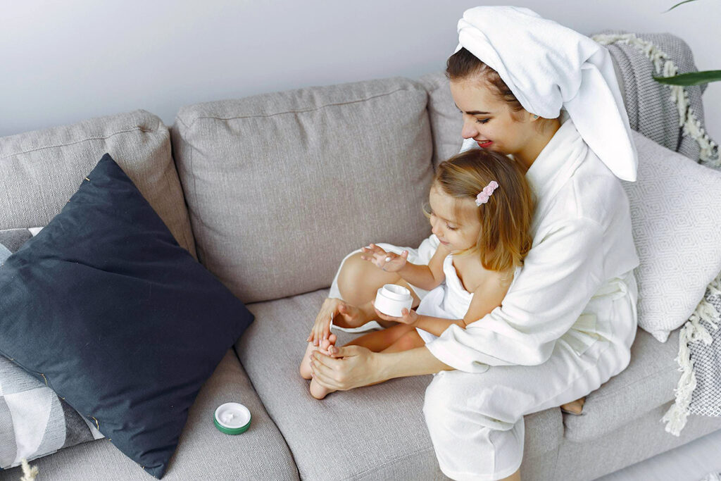 a parent and a daughter sitting on a couch and doing beauty care