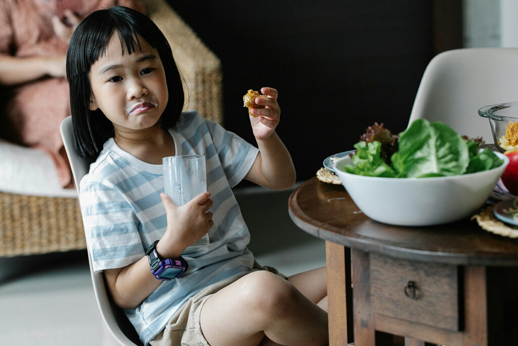 a kid eating nugget and drinking milk in a not so happy mood