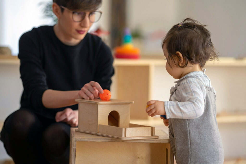 a kid playing in montessori school with card boards while teacher is assisting