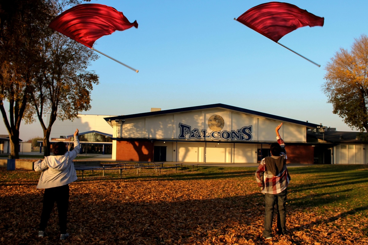 Two kids twirling flags in front of their school.