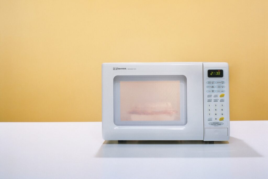 A microwave cooks a meal against a yellow background.