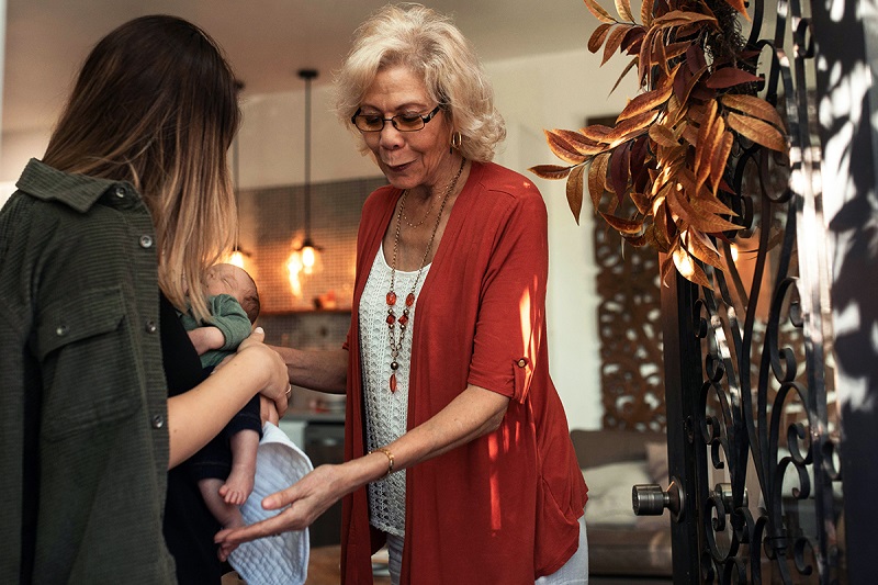 a parent is standing holding the newborn and a grandparent is trying to help