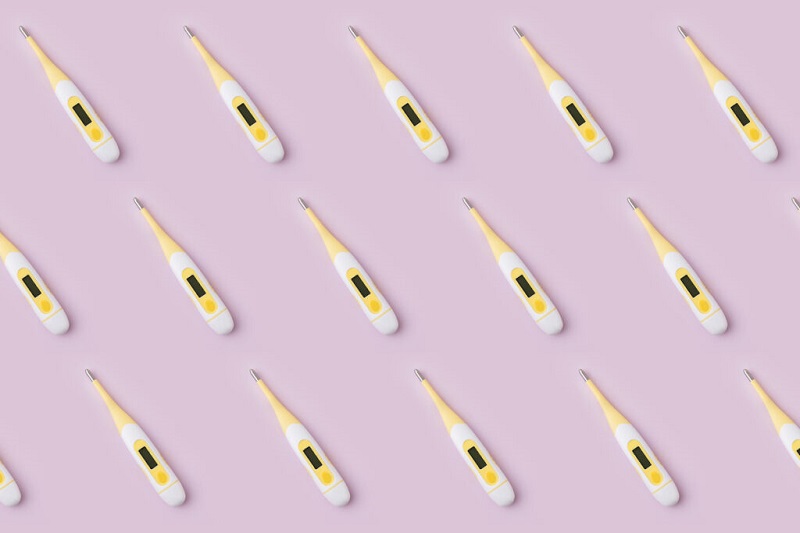 White and yellow digital thermometers are arranged in rows on a pink background.