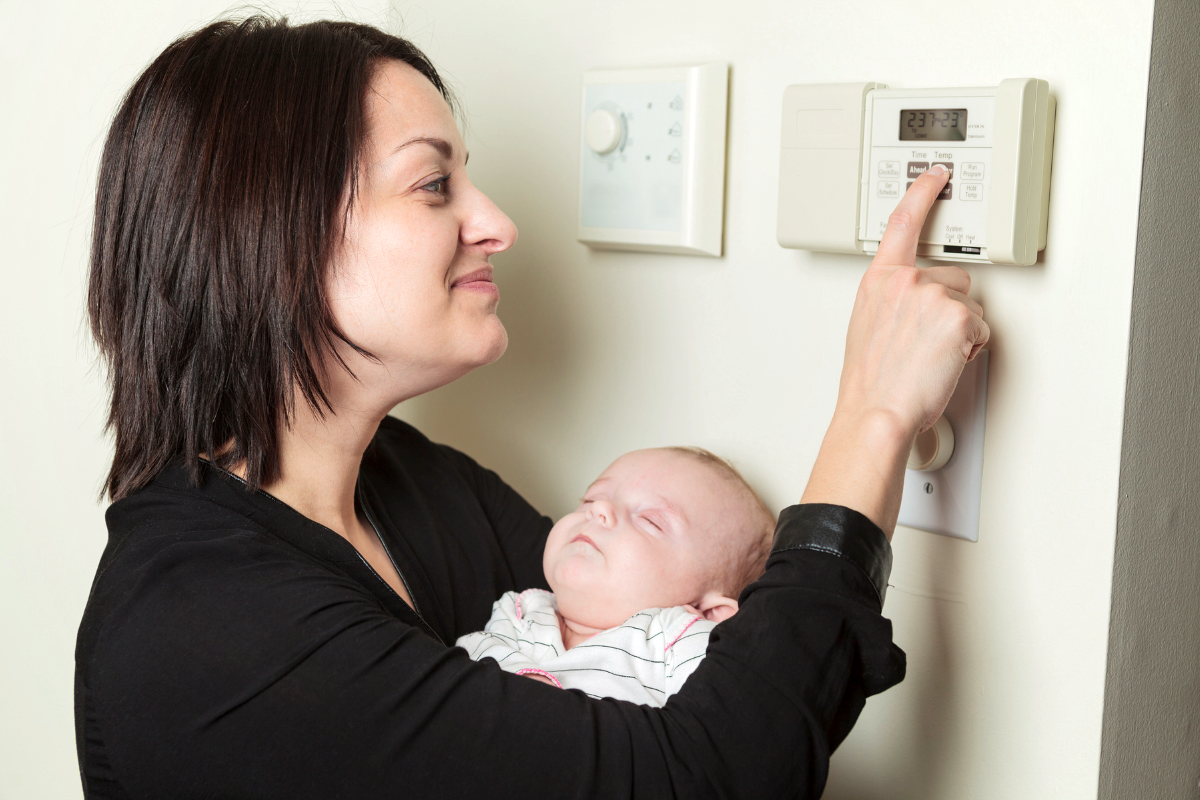 A parent holding a baby and adjusting the thermostat