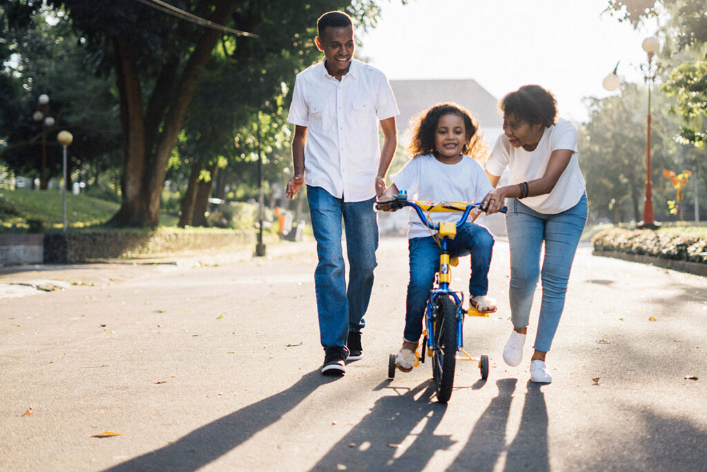 Two parents teaching a kid to drive a bike