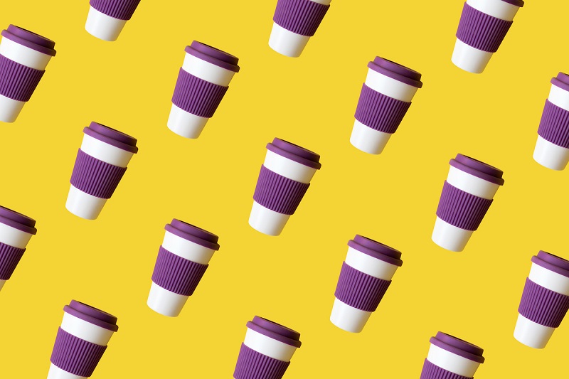 Reusable coffee cups with purple silicone lids and sleeves on a yellow background.