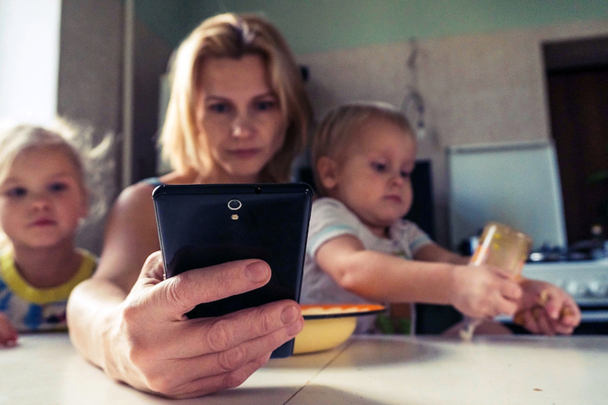 A parent looking at the phone with two kids