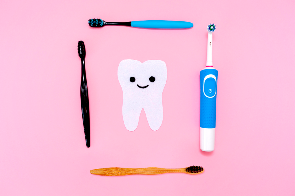 Four toothbrushes laid around a paper tooth on a pink background.