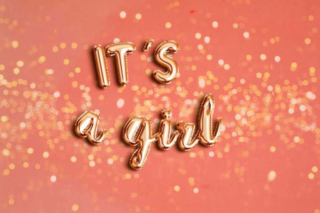 Gold balloons spell out "It's a girl" on a pink background.