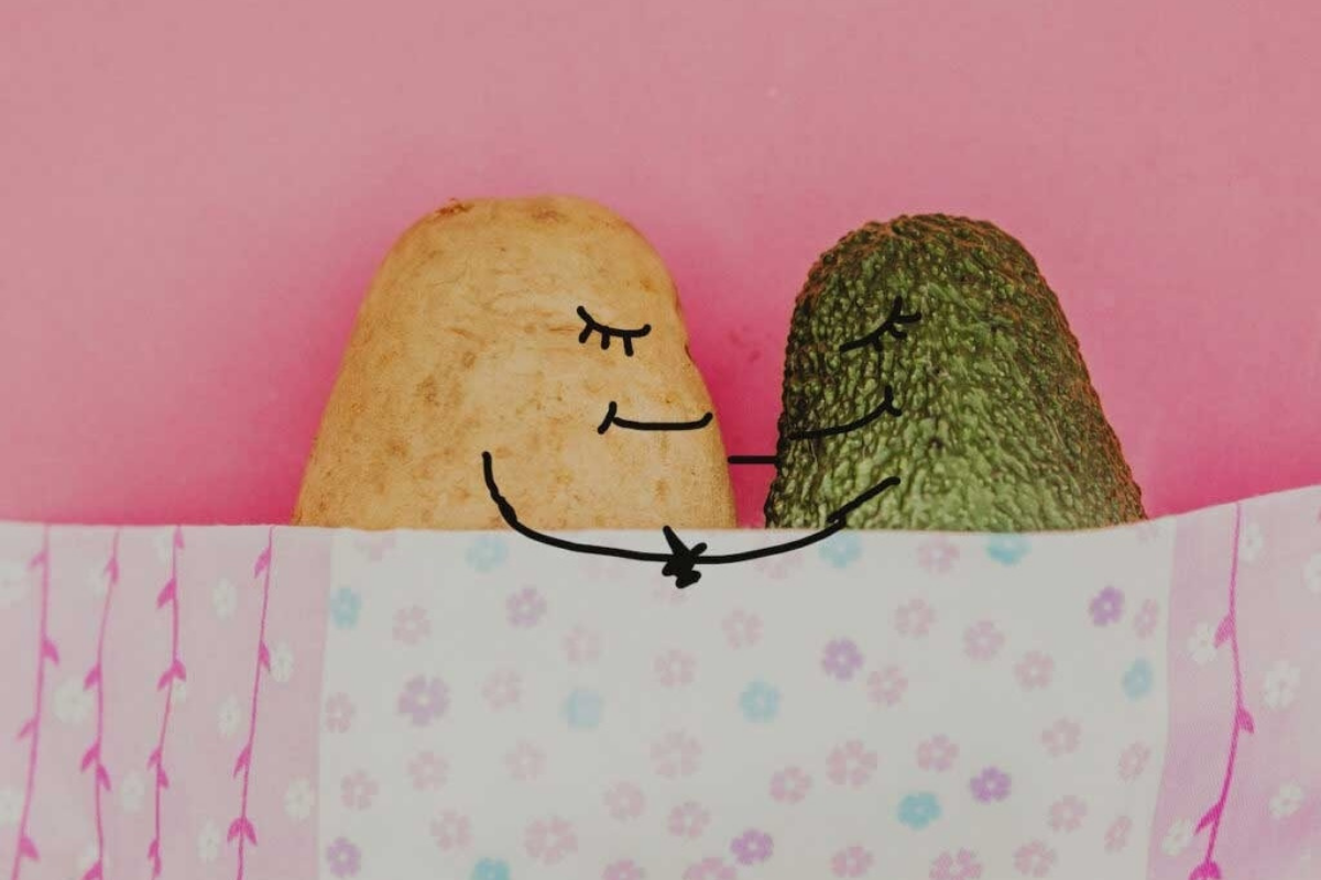 A potato and a cucumber hugging each other in bed.