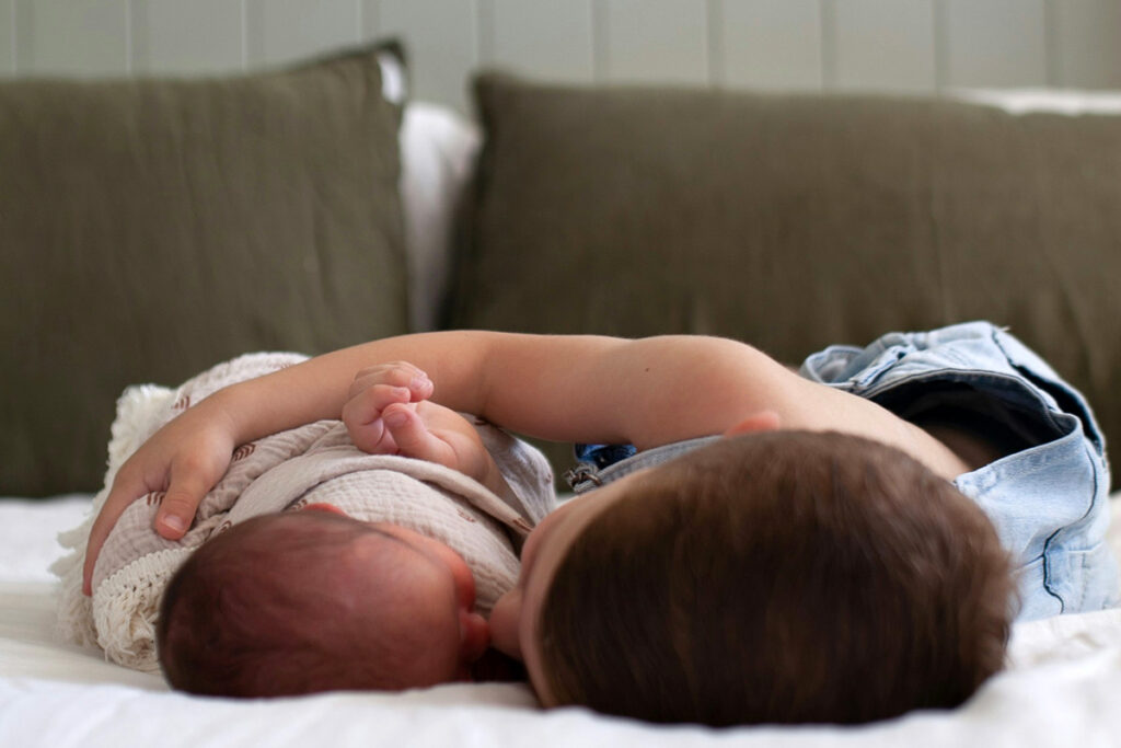 A kid and a baby lying together on a bed embracing each other