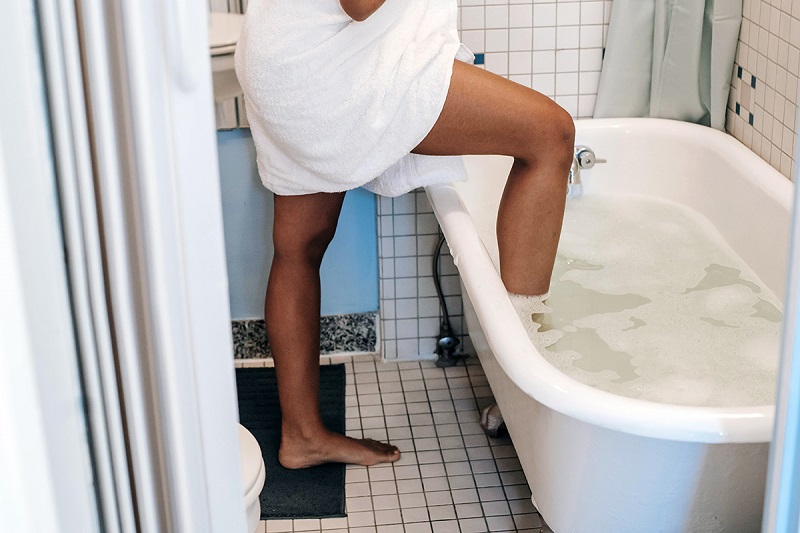 a pregnant adult stepping in the hot bath tub in the washroom