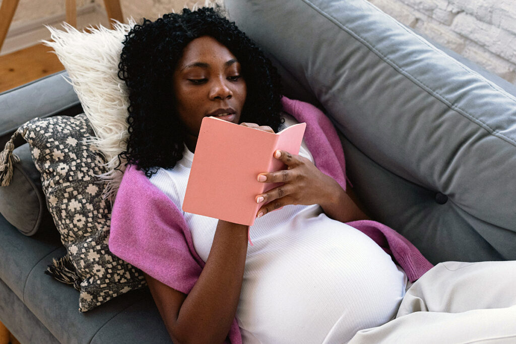 a pregnant adult laying on a sofa and reading a book