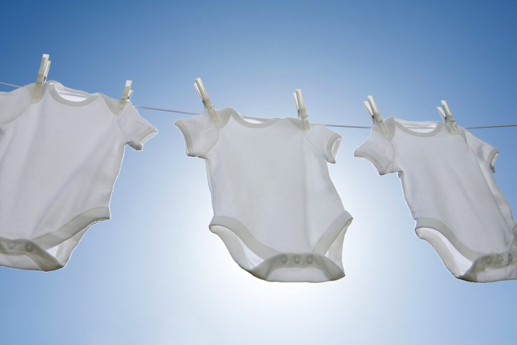 A row of three white onesies on a laundry line on a sunny day.