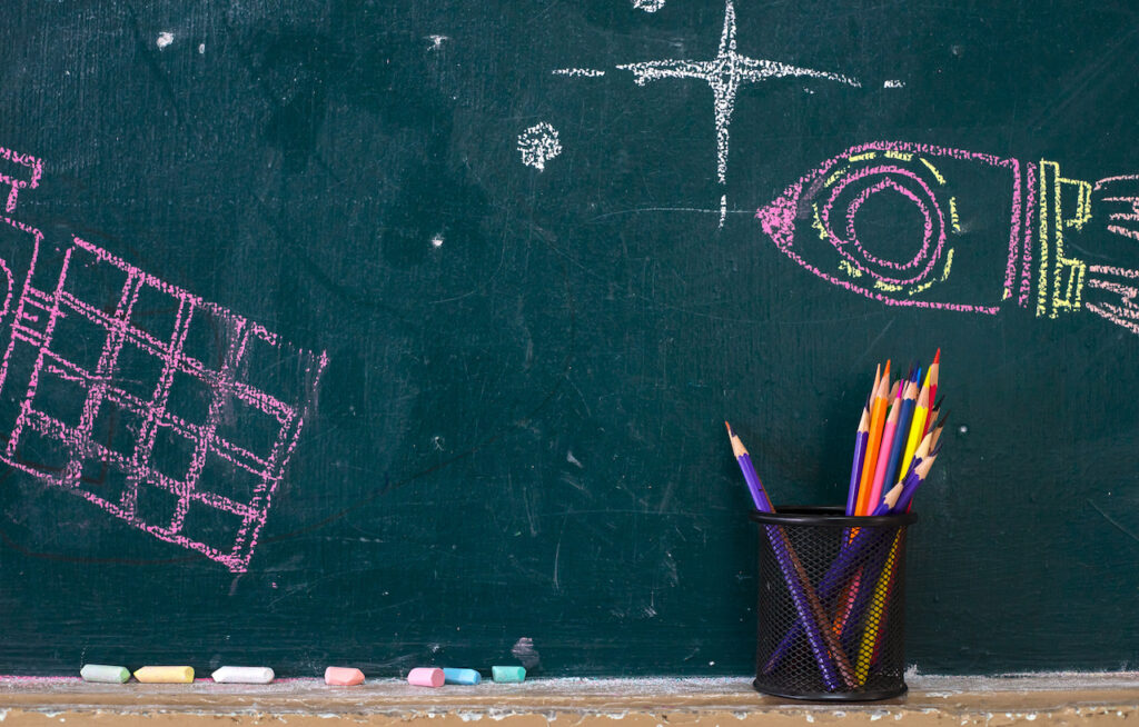 A school chalkboard is covered with drawings of rockets and stars.