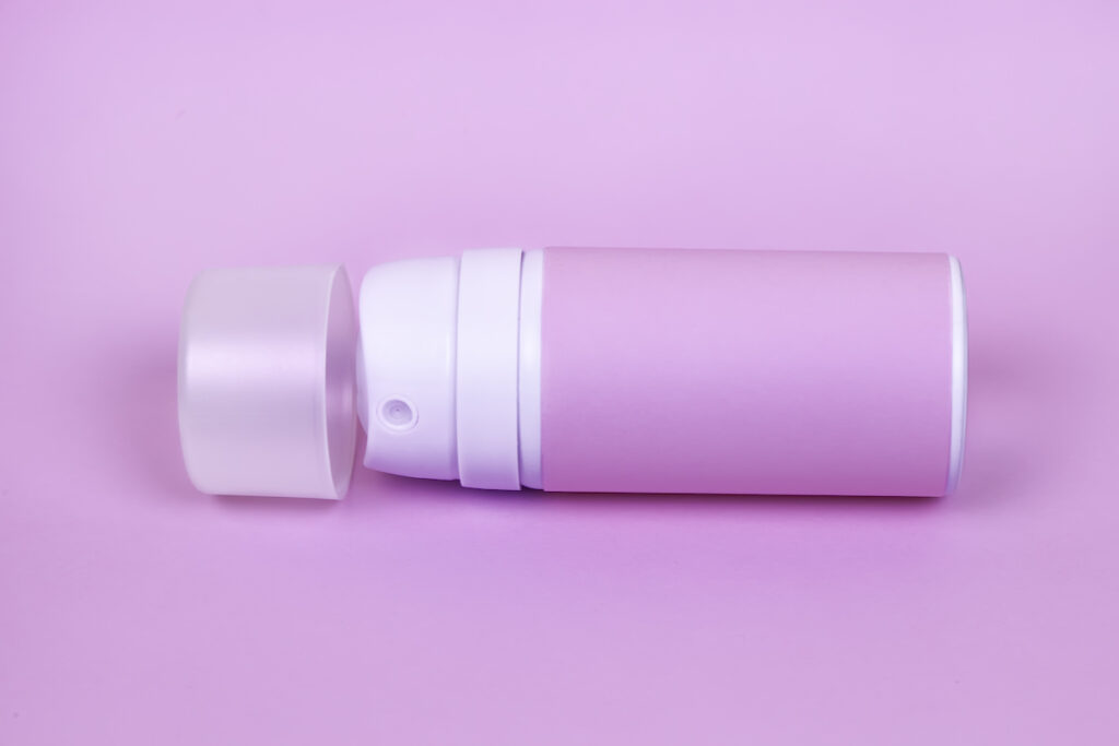A pink aerosol deodorant can on its side on a pink background.