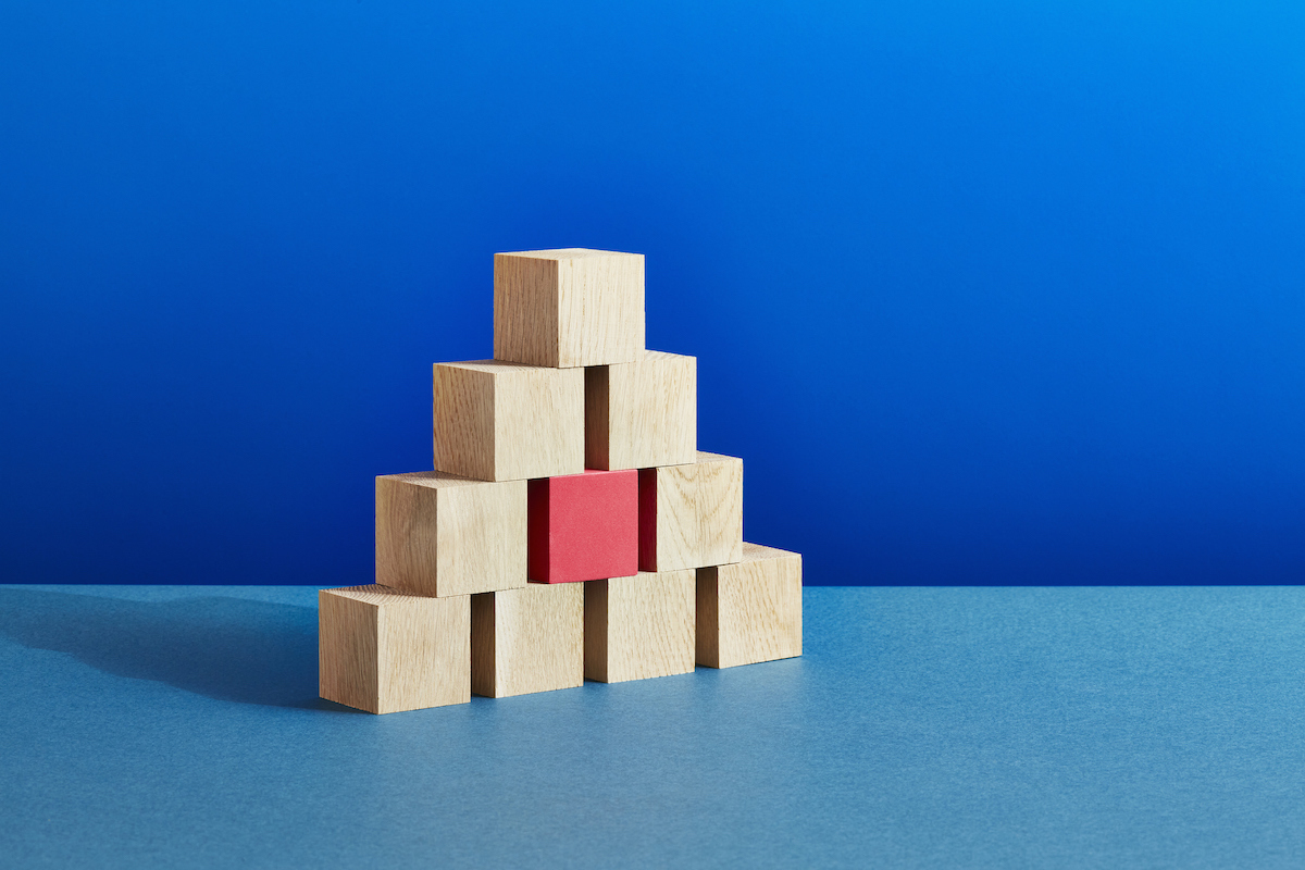 A pyramid of plain wooden block and one red one on a blue background.