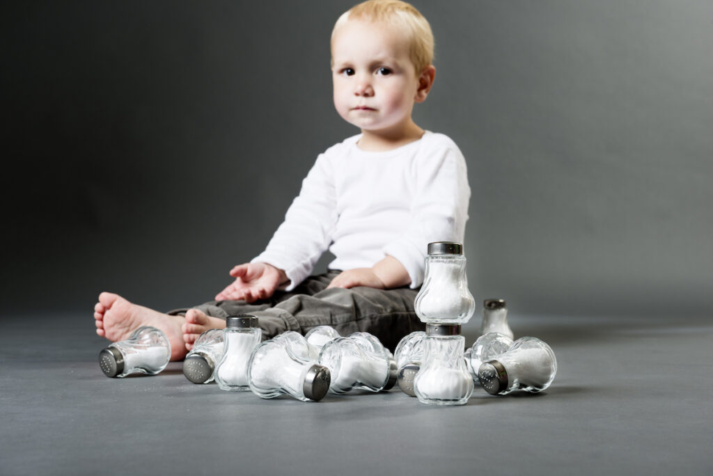 A baby sits with a pile of salt shakers looking stern.