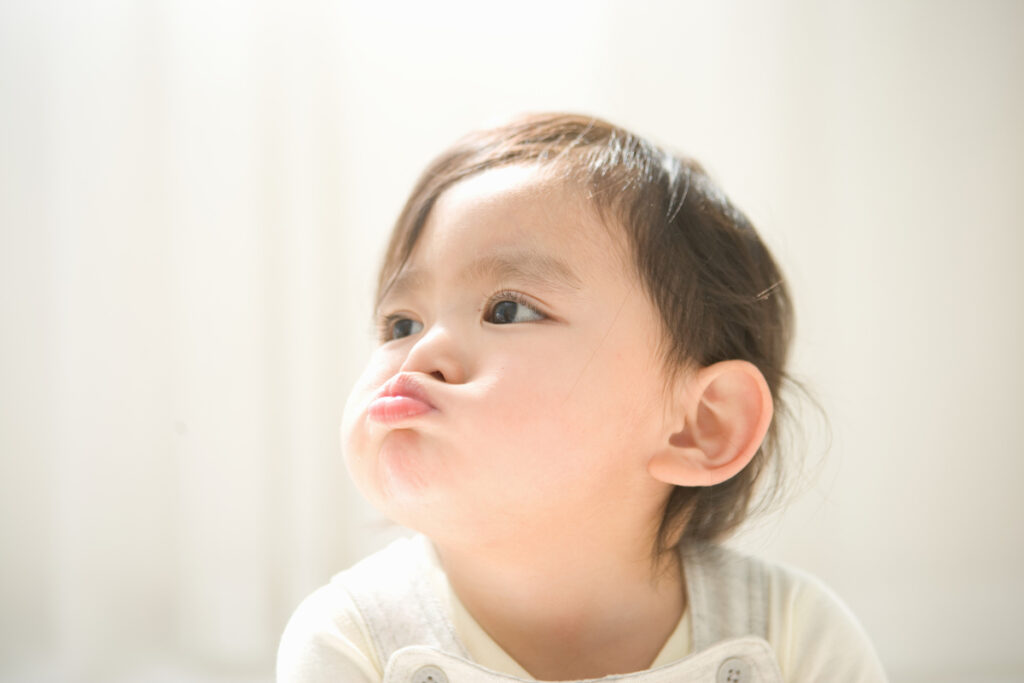 A baby holding their breath with puffed-out cheeks and lips.