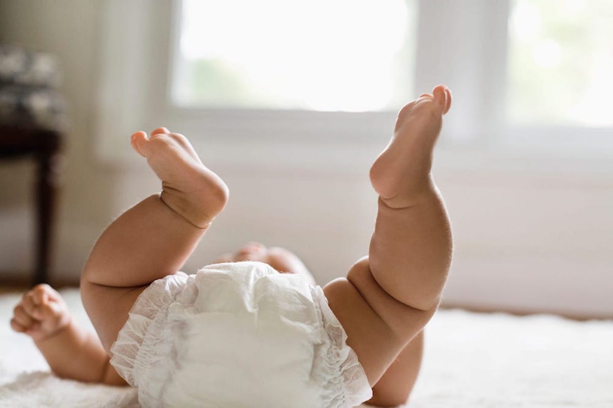 A baby wearing a diaper holds its feet in the air while laying on its back.