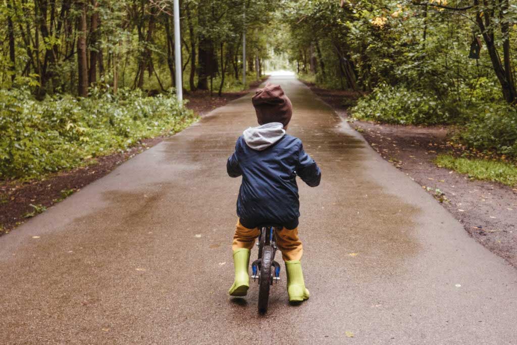 A rear view of a child riding a balance bike down a muddy path.