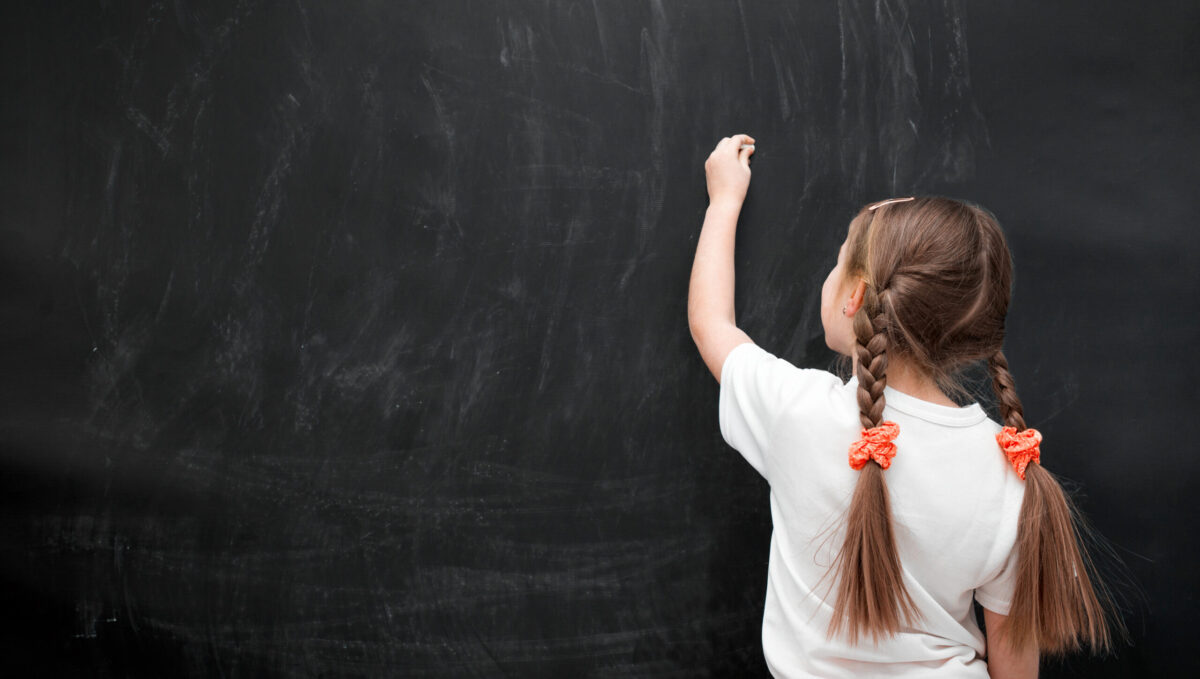 A girl stands in front of a chalkboard, about the draw something.