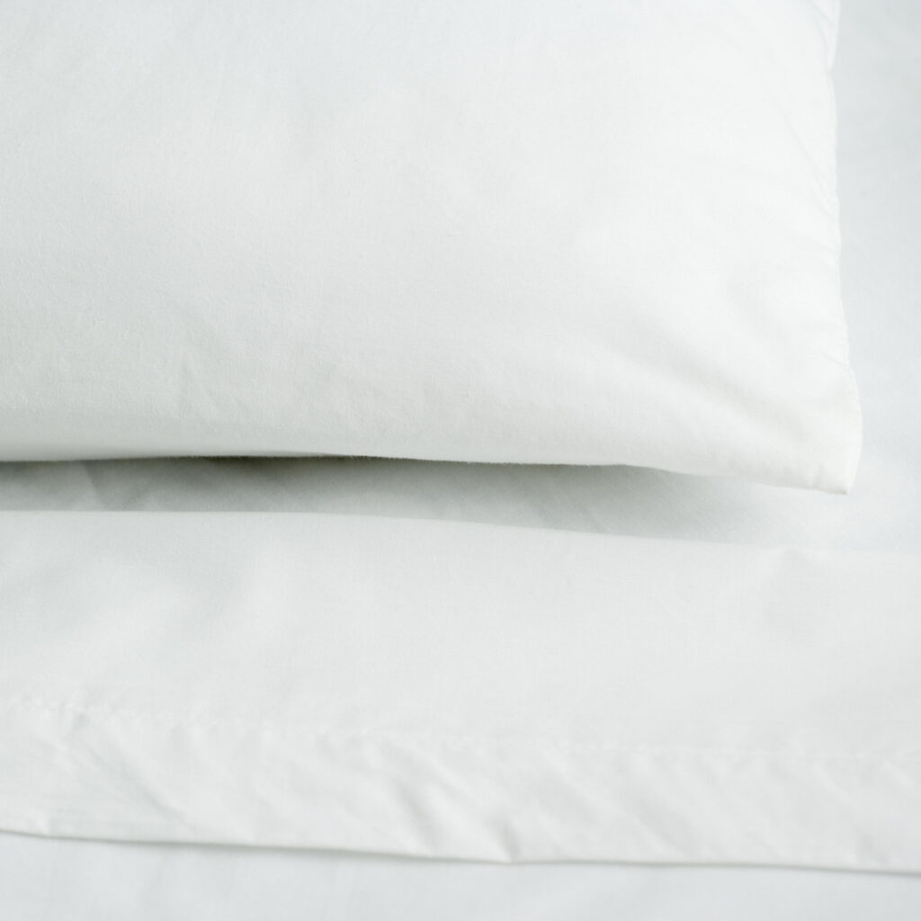 A stack of white pillows on the corner of a bed.