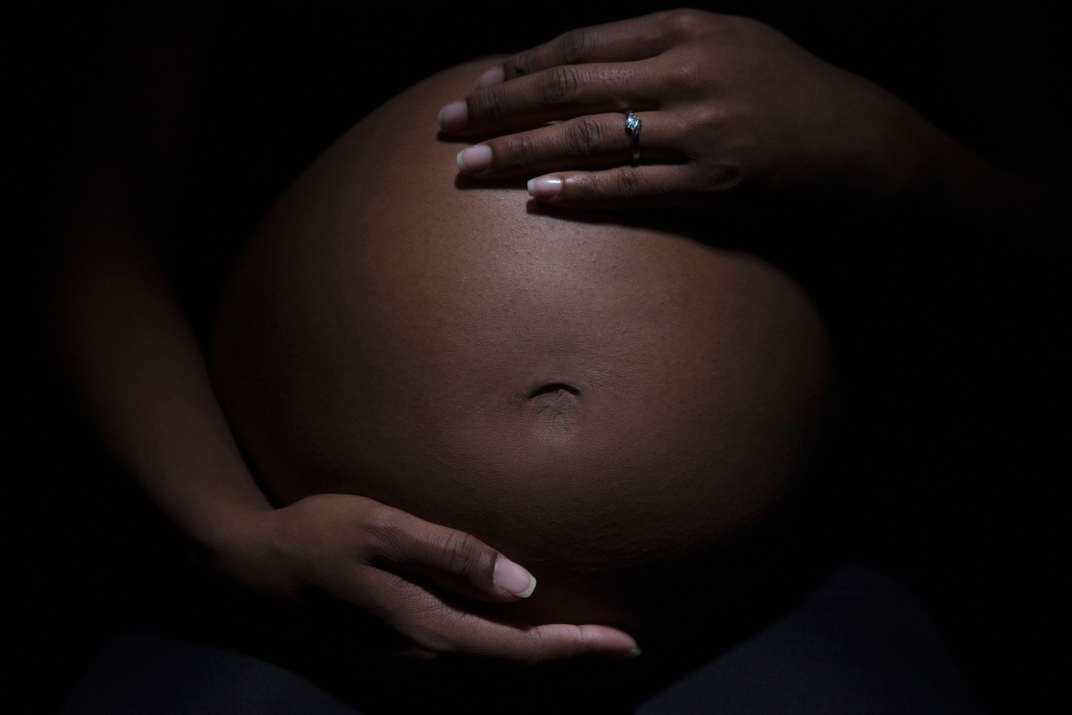 A close up of a Black woman holding her pregnant belly.