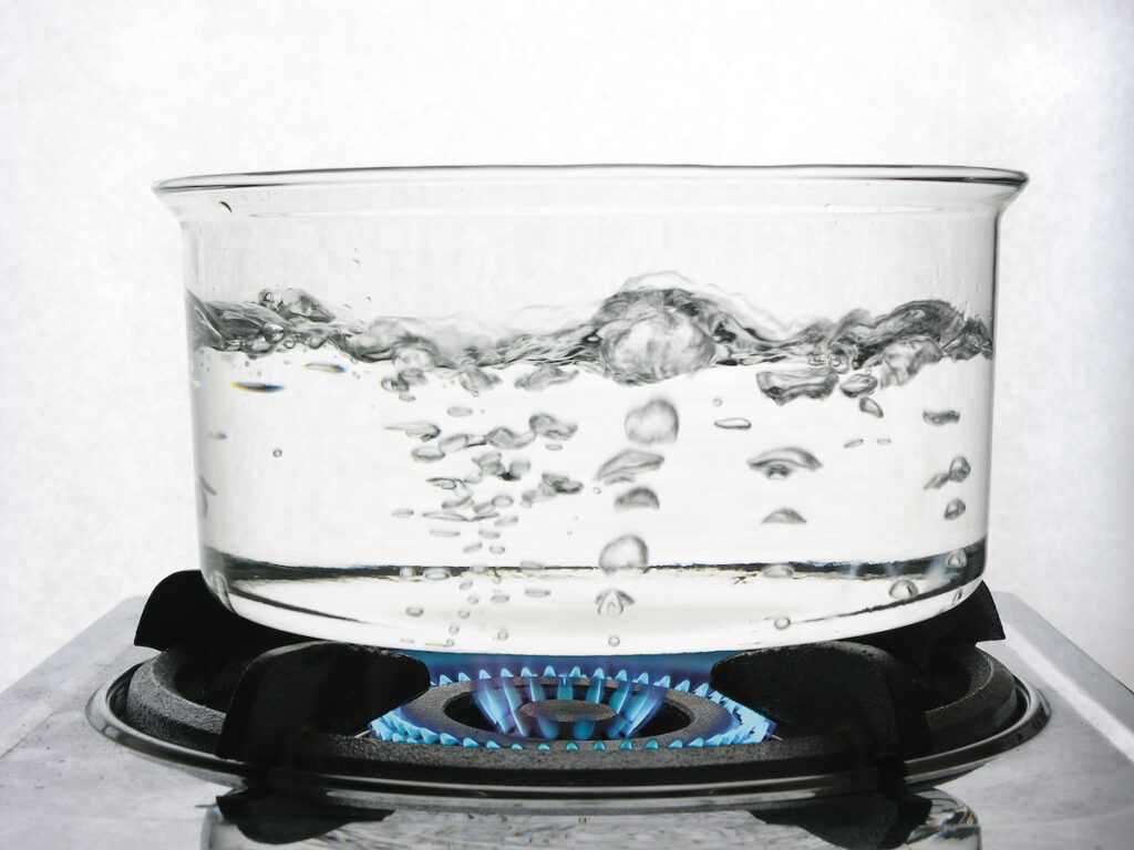 Water boils in a clear pot on a gas stove.