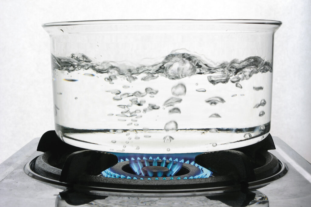Water boils in a clear pot on a gas stove.