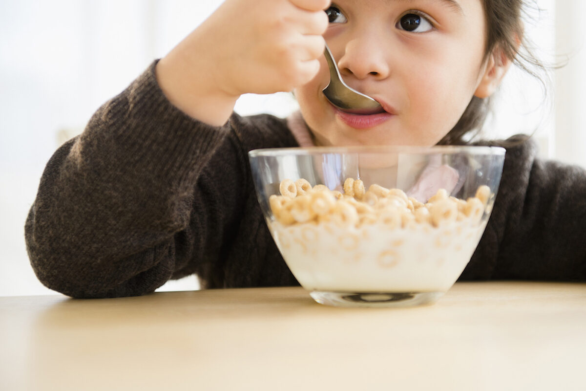 Child eats cereal and milk out of a clear glass bowl.