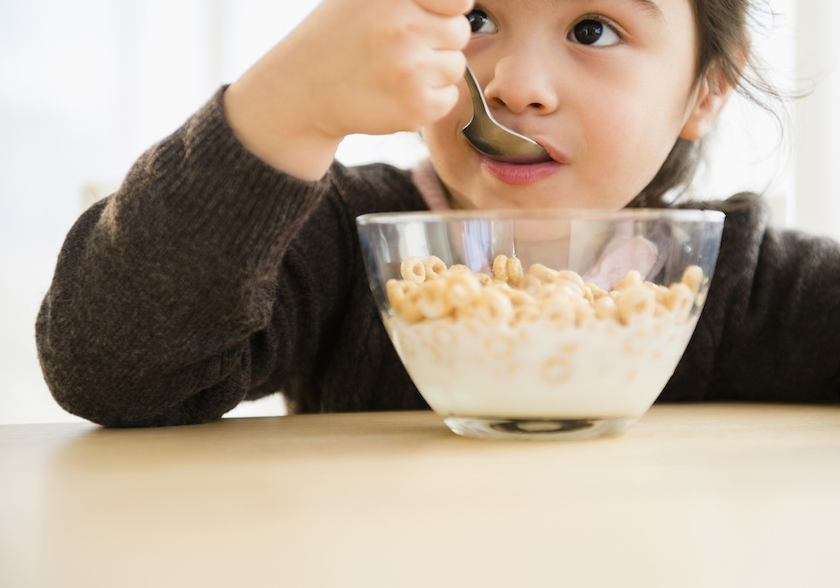 Child eats cereal and milk out of a clear glass bowl.