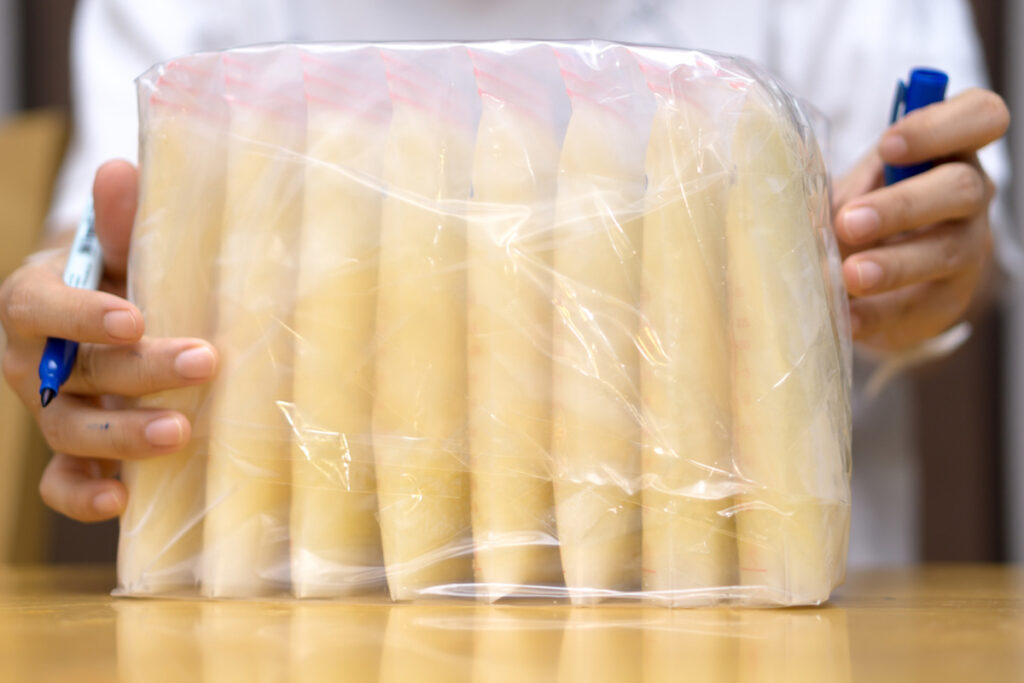 A stash of filled breast milk freezer bags is seen with a hand on either side of the bag.