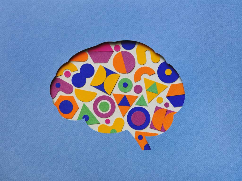 Paper craft illustration of brain filled with multi colored geometric shapes.