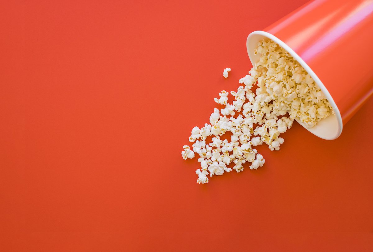 A high-angle view of popcorn spilled across a orange-red background.