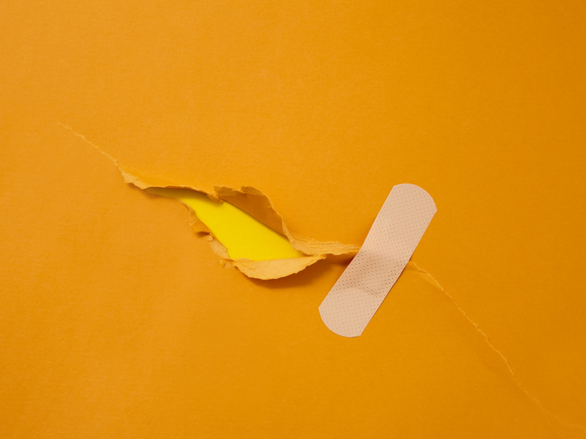 A bandaid is applied over a tear in a piece of orange paper.