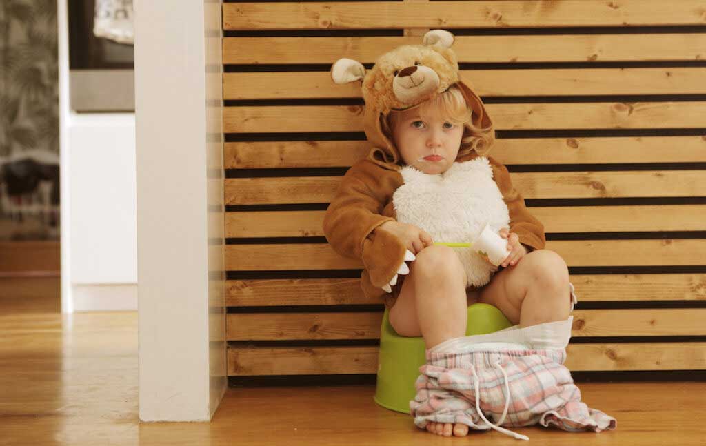 Distressed toddler eating yogurt while sitting on a training potty and dressed as a bear.