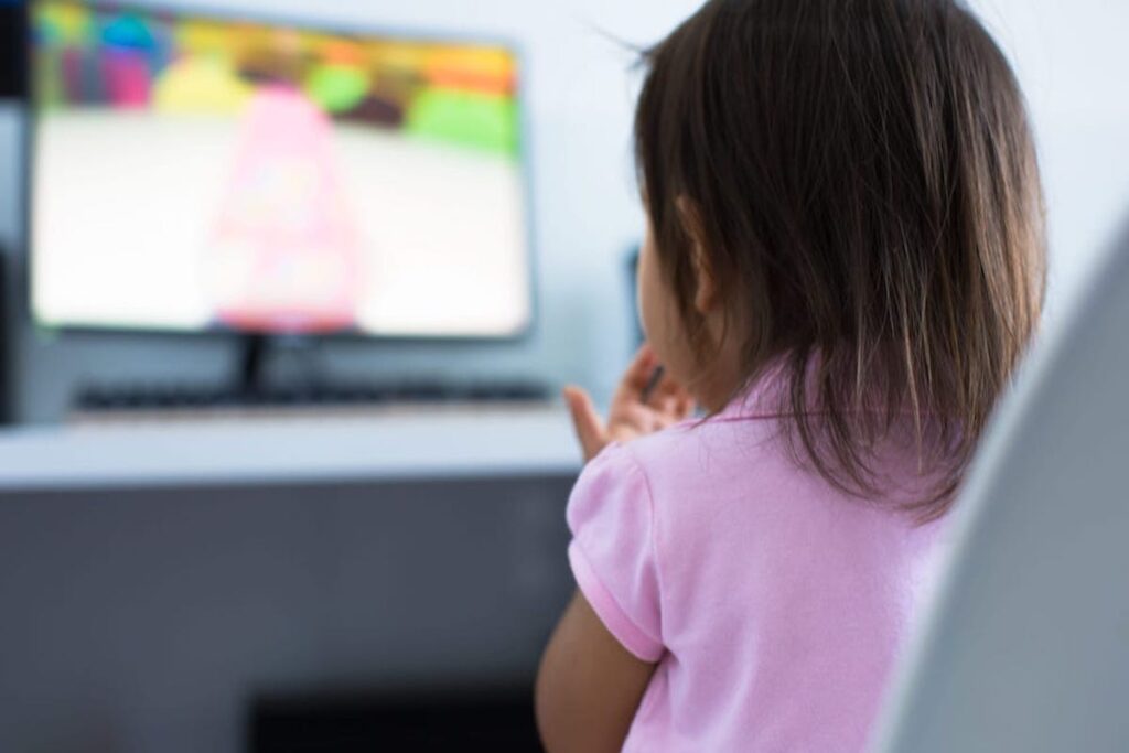 A child in a pink shirt stands in front of a television screen.