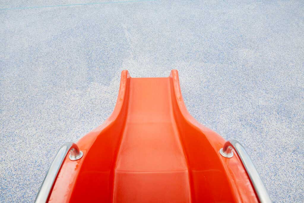 A high-angle view of a red slide leading to gray concrete.