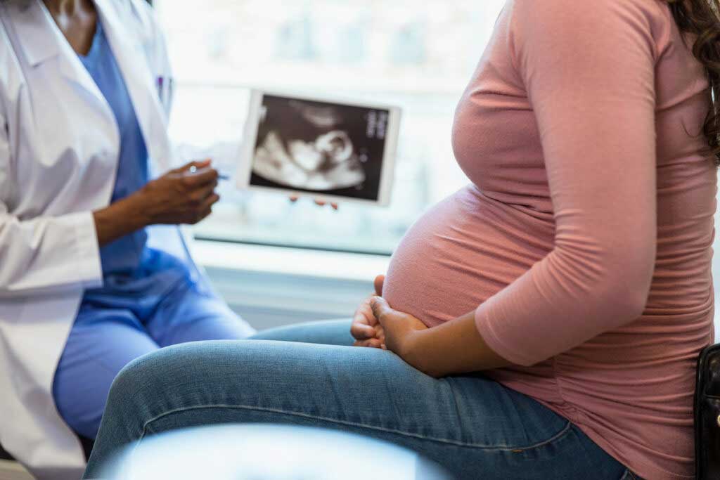 A pregnant person consults with a doctor, who is holding up an image from a sonogram.